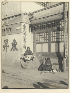 Seamstresses sewing outdoors next to a hostel and a building with a sign offering to buy pawn tickets and second-hand clothing