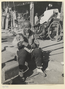 Seated man holding a child with a rickshaw in the background