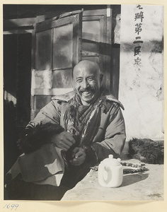 Man sitting outdoors next to a teapot and an inscription on a building
