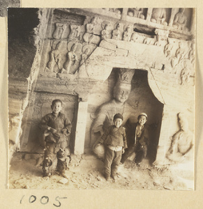 Three boys standing in front of a niche with a seated Bodhisattva and wall with thousand Buddha relief in Cave 30 at Yun'gang