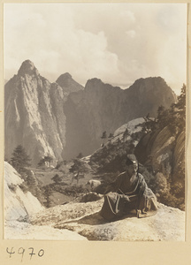 Daoist priest wearing formal dress and holding a yak-tail fly whisk on East Peak of Hua Mountain with Qinling Mountains in background