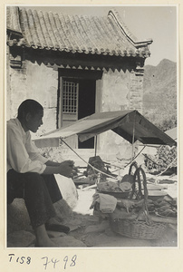 Man sitting next to baskets of food, sedan chair with awning, and building on Tai Mountain