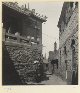 Man in a street next to a stone building with roof ornaments in a village on the Shandong coast