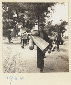 Member of a funeral procession carrying a paper figure of a cook with baskets