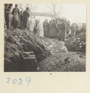 Members of a funeral procession in front of vaulted brick tomb strewn with paper money