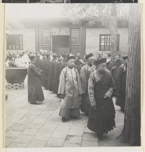 Mourners and monks with musical instruments in courtyard during funeral