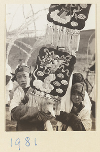Boys carrying fan-shaped banners with apliquéd and embroidered figures in a funeral procession