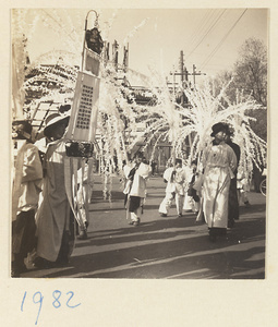 Members of a funeral procession carrying paper snow willows and an inscribed banner