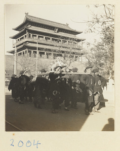Members of a funeral procession carring a wreath in front of a city gate
