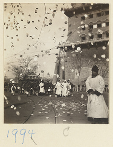 Members of a funeral procession carrying coffin and throwing paper money in the air in front of city gate