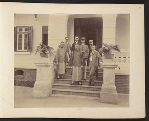 Two Chinese men in traditional dress posing with five foreigners on steps in front of building in Canton