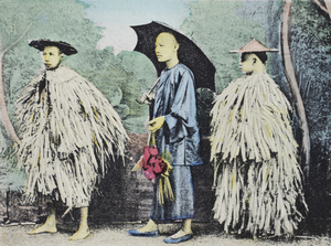 Three men posed in a photographer's studio – two wearing palm leaf raincoats and bamboo hats