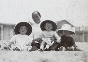 Amah with three children wearing pith helmets on a beach