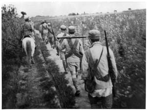 Soldiers walking past a field 