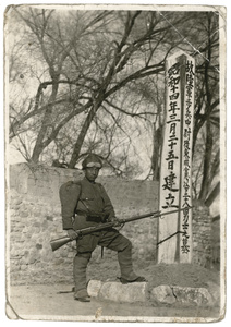 A soldier with bayonet on rifle beside the grave of twenty-eight Japanese infantrymen