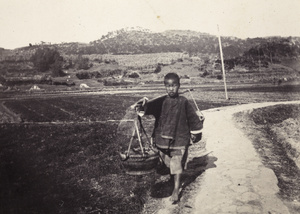 A boy carrying baskets balanced on a bamboo yoke