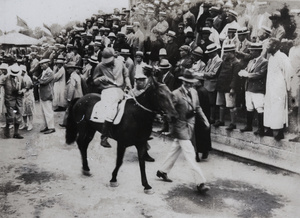 A man leading a horse and jockey past a viewing stand