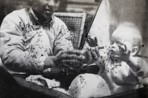 An amah playing with a baby in a pram
