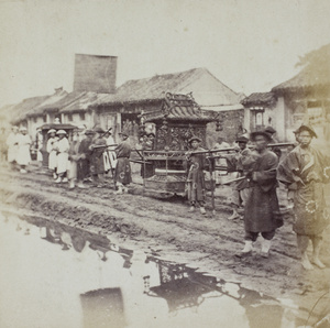 A funeral procession along a muddy road, carrying a paper pavillion