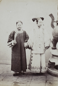 A Manchu woman with her maid, standing beside a large bronze burner, Beijing