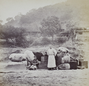 Two men beside River Min, with items including John Thomson's photographic equipment, after running aground on rapids